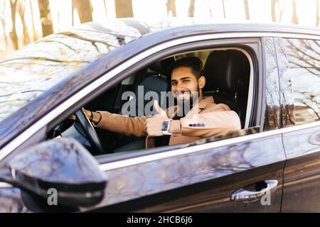 Young asian man smiling and showing thumb up in his car. Stock Photo