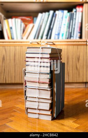 stack of old books tied with rope on parquet floor near bookcase Stock Photo