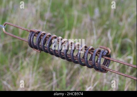 Rusty spring connecting parts of a rural fence to protect animals Stock Photo