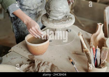 Close-up of woman putting hands in bowl with water and making vase from clay on the equipment Stock Photo