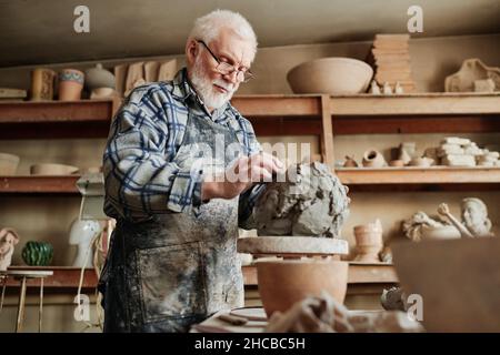 Senior male ceramist working with clay and making dishes by hands in pottery studio Stock Photo