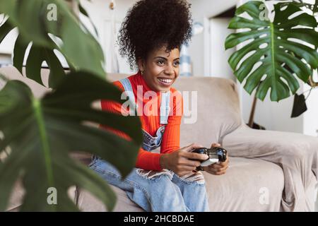 Happy curly haired woman playing video game on sofa Stock Photo