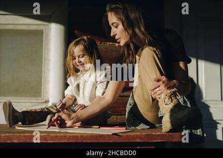 Smiling girl drawing with woman in book at bench Stock Photo
