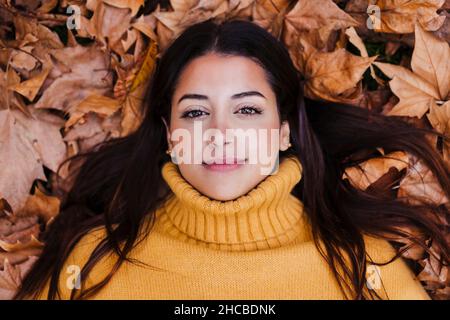 Young woman wearing sweater lying on dry autumn leaf Stock Photo