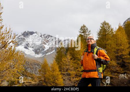 Smiling senior man with backpack hiking at Rhaetian Alps, Italy Stock Photo