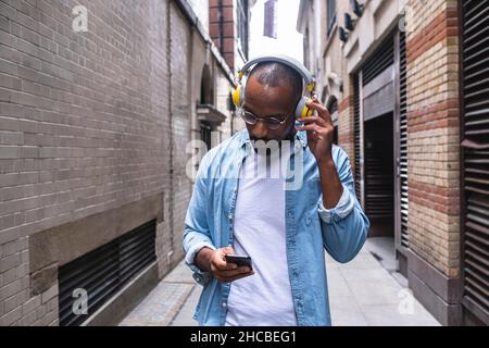 Man with headphones using smart phone walking in alley Stock Photo