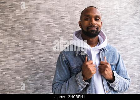Smiling man with denim jacket standing in front of wall Stock Photo