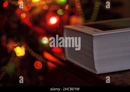 thick book on the background of a christmas tree with christmas lights. Stock Photo
