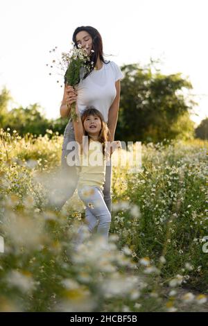 Mother smelling bunch of flowers held by daughter in meadow Stock Photo