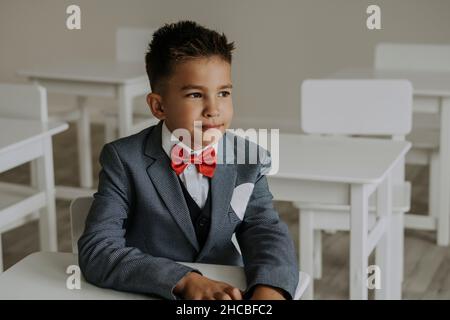 Schoolboy wearing red bow tie with suit sitting in classroom Stock Photo