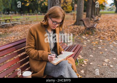 Young woman writing in book in public park Stock Photo
