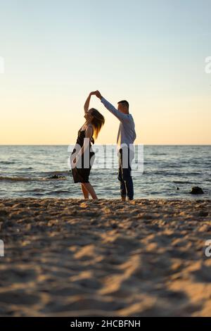 Young couple dancing together on sand at sunset Stock Photo
