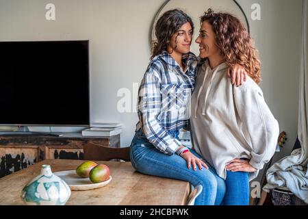 Happy mother looking at daughter sitting on dining table at home Stock Photo
