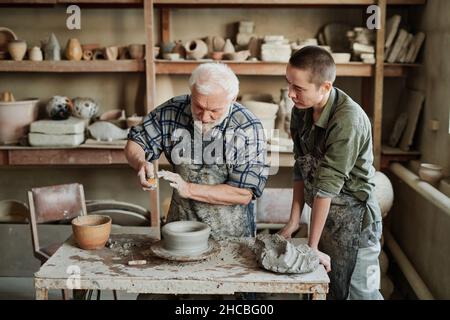 Senior man showing the process of making ceramic vases to his assistant in the pottery workshop Stock Photo
