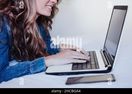 Smiling young woman using laptop in bedroom Stock Photo