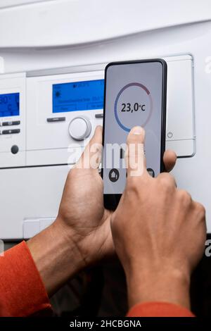 Man adjusting boiler temperature through mobile phone at home Stock Photo