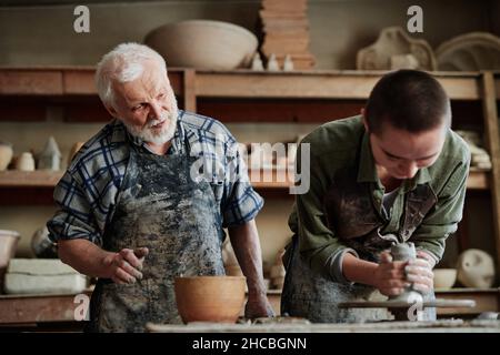 Young woman learning to make ceramic vase on pottery wheel in studio together with teacher Stock Photo