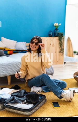 Happy young woman packing suitcase in bedroom Stock Photo
