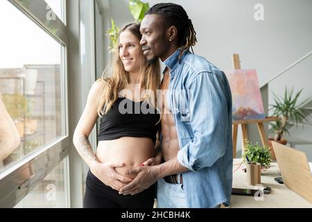 Happy couple expecting baby looking at belly of pregnant woman at home Stock Photo