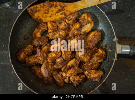 Homemade spicy and tasty chicken ghee roast cooked in a pan and placed on a shiny black marble counter top. Mangalorean spicy chicken dish. Stock Photo