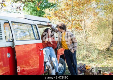 Smiling man leaning on van talking with woman at campervan Stock Photo
