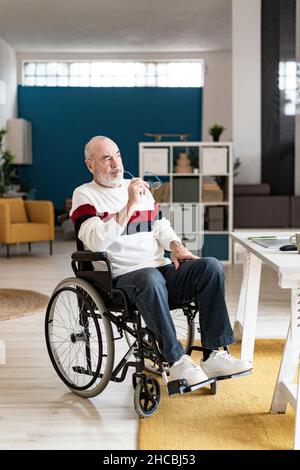 Smiling disabled freelancer holding coffee mug sitting at desk in home office Stock Photo