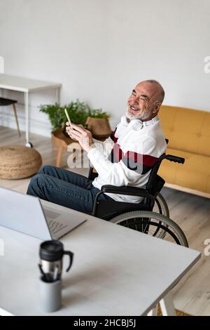 Smiling disabled man with headphones using mobile phone at home office Stock Photo