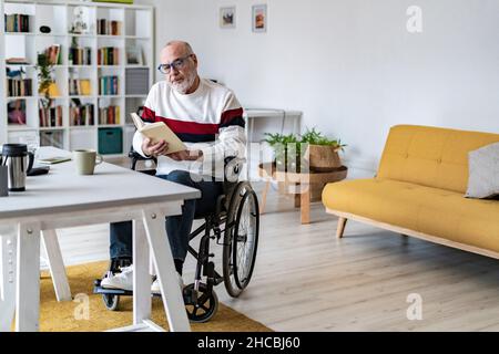 Serious senior businessman on wheelchair reading diary at home office Stock Photo