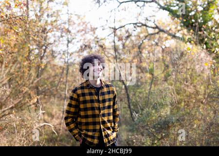 Curly haired man with hands in pockets smiling at forest Stock Photo
