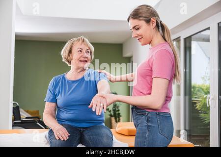 Young physiotherapist helping patient to stretch hand at home Stock Photo