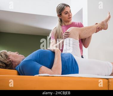 Physiotherapist helping disabled woman to exercise leg on massage table Stock Photo