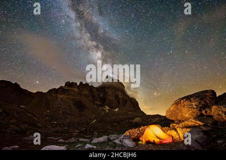 Milky Way galaxy stretching against night sky over lone illuminated tent in Maira Valley Stock Photo