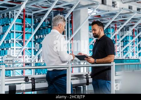 Warehouse manager discussing over tablet PC with businessman in industry Stock Photo