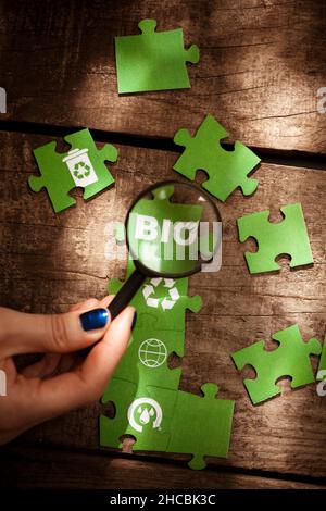Woman holding magnifying glass over Bio text on green puzzle piece Stock Photo