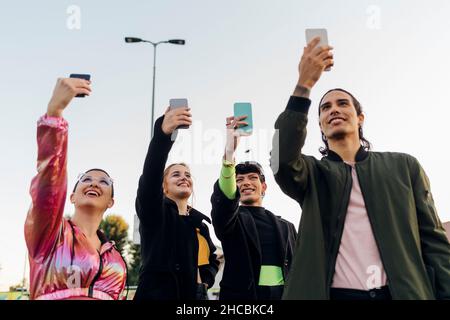 Smiling friends taking selfies through smart phones together Stock Photo