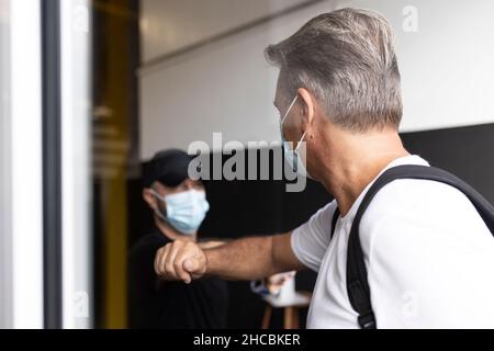 Man taking temperature of woman wearing protective face mask at doorway Stock Photo