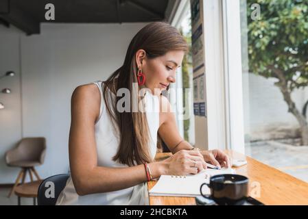Woman writing in diary sitting at cafe Stock Photo