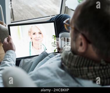 Doctor advising patient on video call through digital tablet at home Stock Photo
