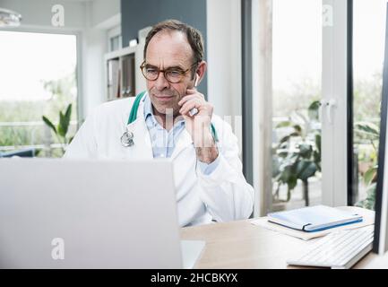 Doctor using laptop concentrating at desk in clinic Stock Photo