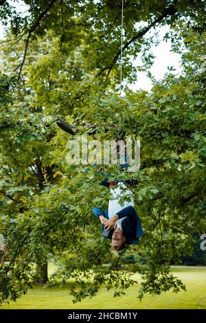 Serious businessman using smart phone sitting on tree branch with rope Stock Photo