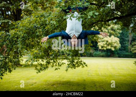 Smiling businessman talking on smart phone relaxing on tree branch with rope Stock Photo