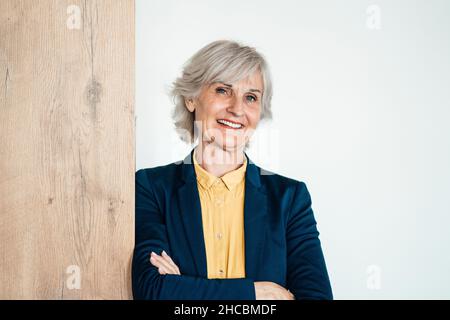 Senior businesswoman with hands behind back in front of white wall Stock Photo