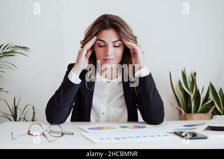 Tired businesswoman with head in hands sitting at desk in office Stock Photo