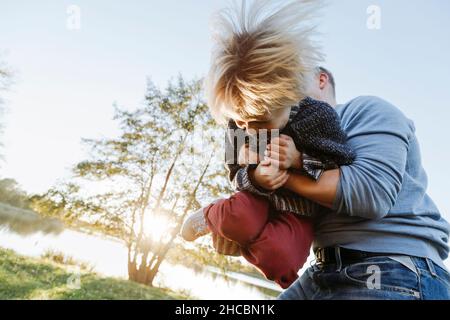 Smiling man holding aloft blond boy flying under clear sky Stock Photo