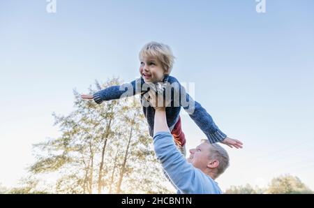 Parents holding cheerful boy upside down at park Stock Photo