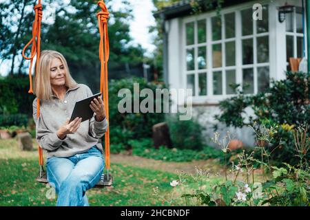 Blond woman using tablet PC at backyard Stock Photo