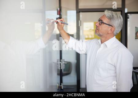 Mature businessman writing on whiteboard in office Stock Photo