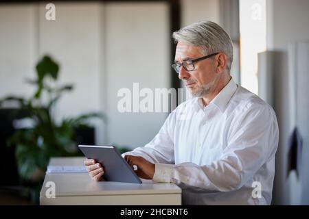Mature businessman working on tablet PC at counter in office Stock Photo