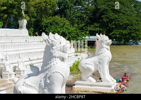 People bathing and washing on the riverbank of Irrawaddy River, next to chinthe statues, Burma Stock Photo