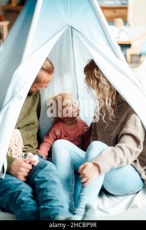 Playful daughter sitting with parents inside tent at home Stock Photo